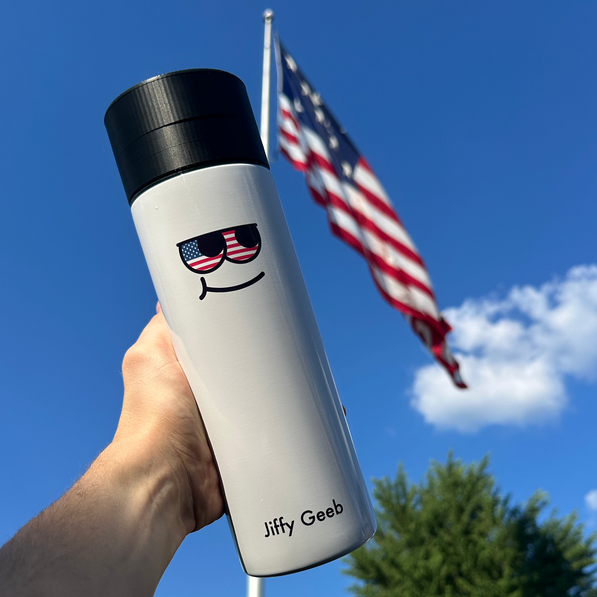 Person holding a white water bottle with a smiley face design against a blue sky with an American flag.